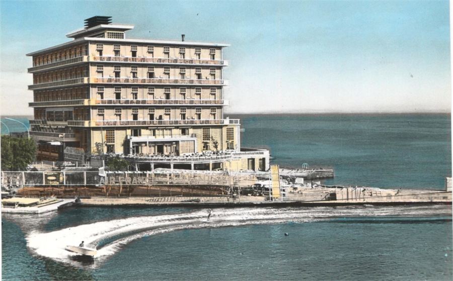 Hand-coloured postcard of the St. Georges Hotel with a waterskier passing the terrace